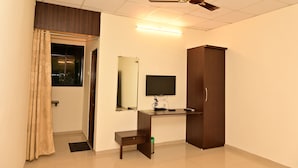 A room with a desk, a television, a wardrobe, a ceiling fan, and a window with curtains. - Tigers Heaven Resort (Chimur)