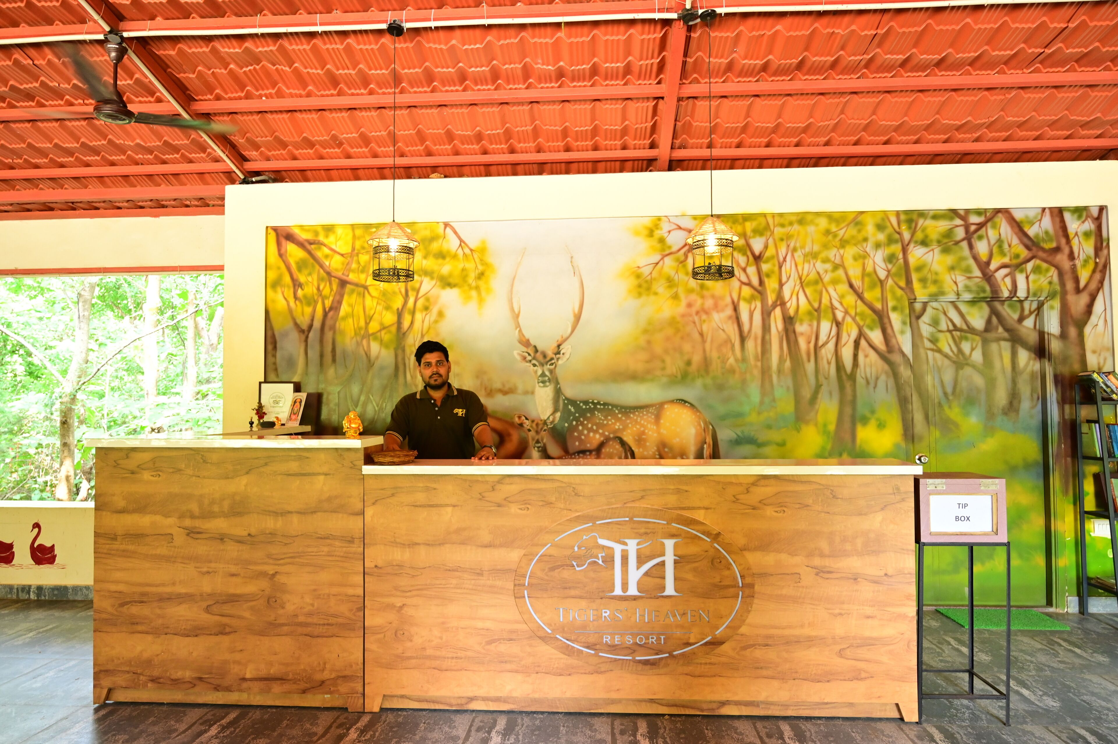 Mostrador de recepción en un resort con un mural de un ciervo y árboles, un logotipo y un cartel para propinas.