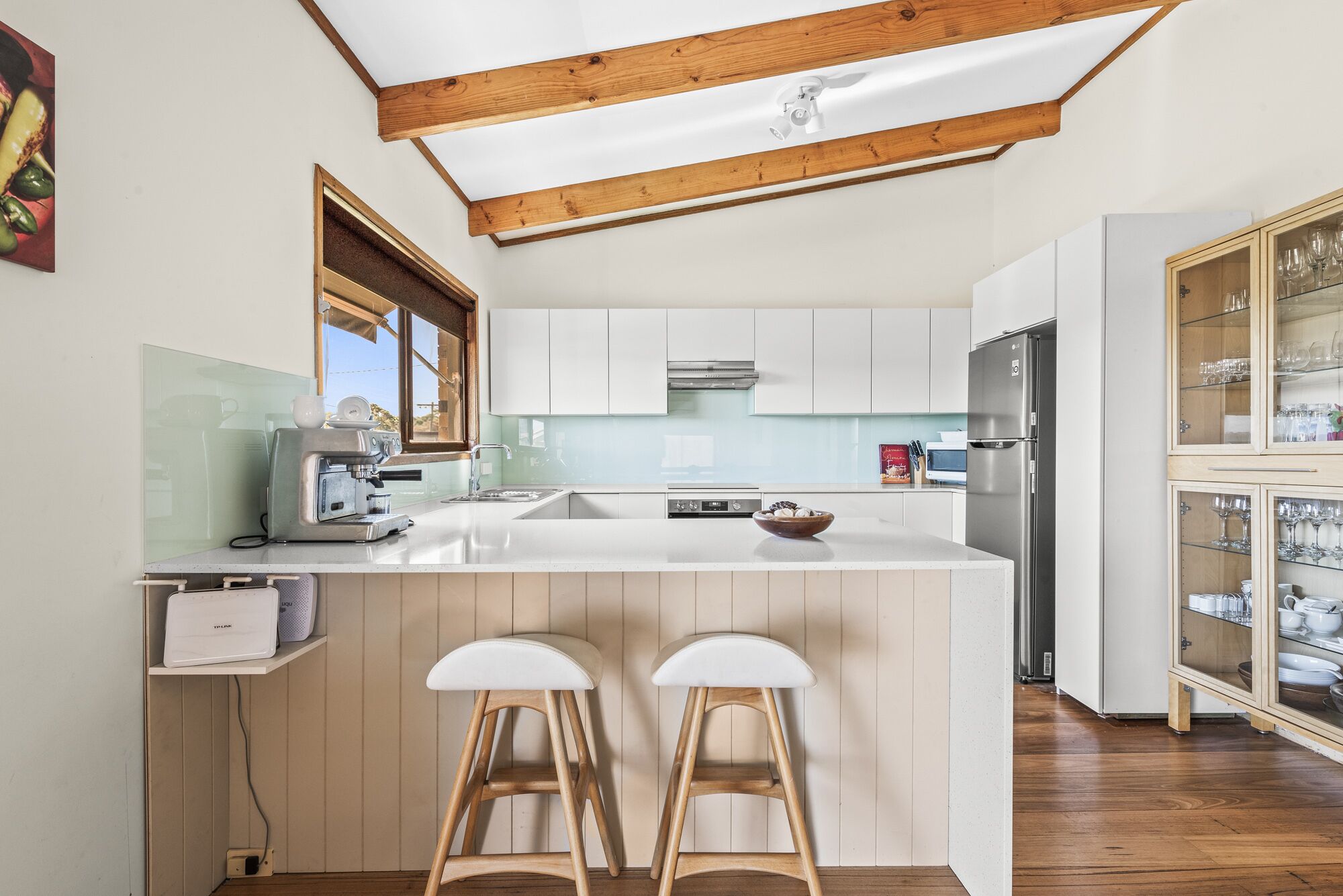 A modern kitchen with white cabinetry, a central island with stools, a built-in espresso machine, and a wine cabinet.