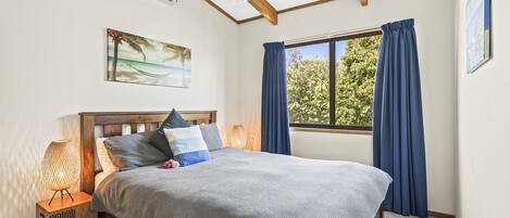 A bedroom with a bed, a window with curtains, a painting on the wall, and an air conditioning unit.