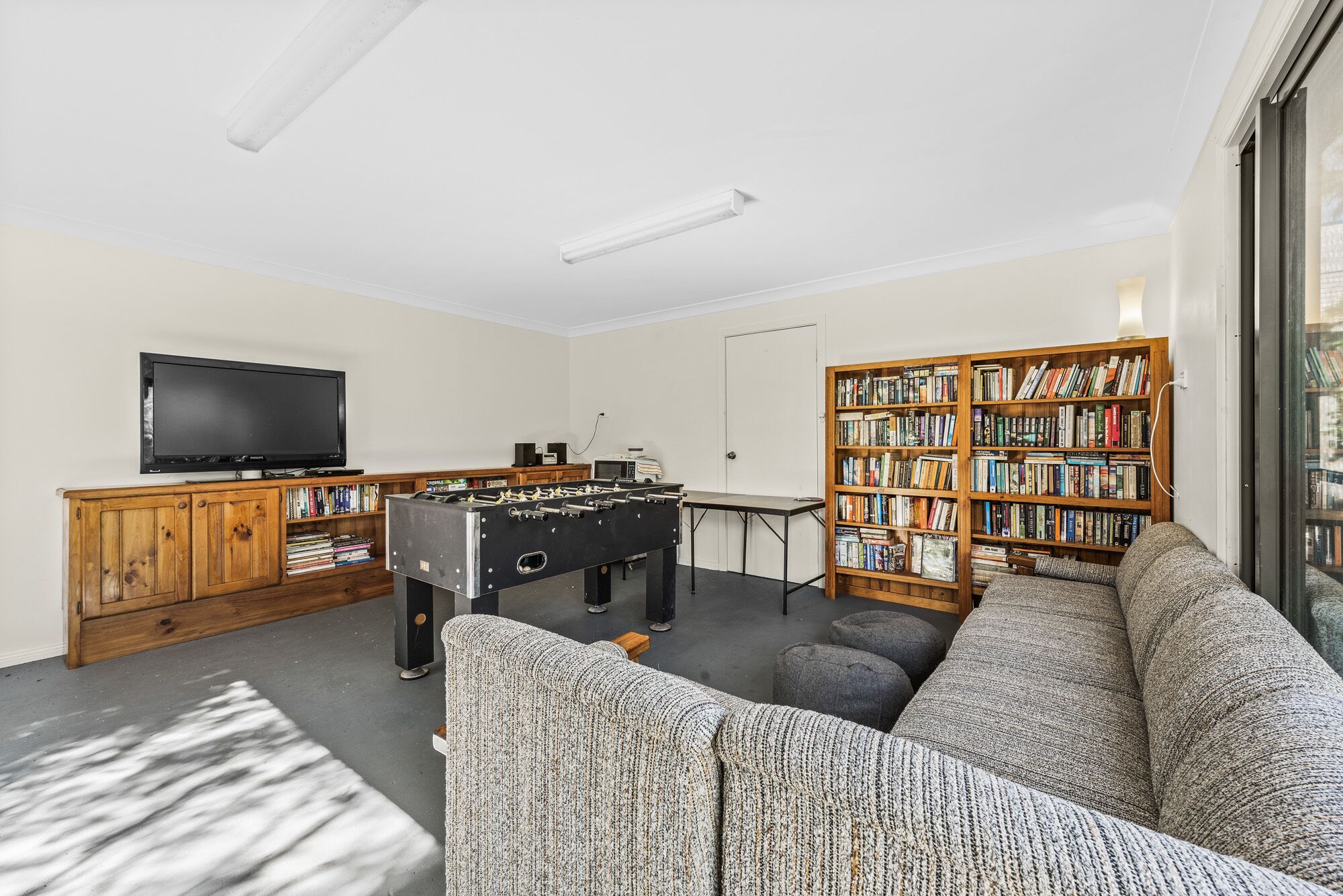 A living room with a foosball table, a television, a bookshelf, and a sofa.