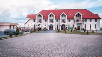 A large, white building with a red roof and multiple windows. There is a paved driveway in front.