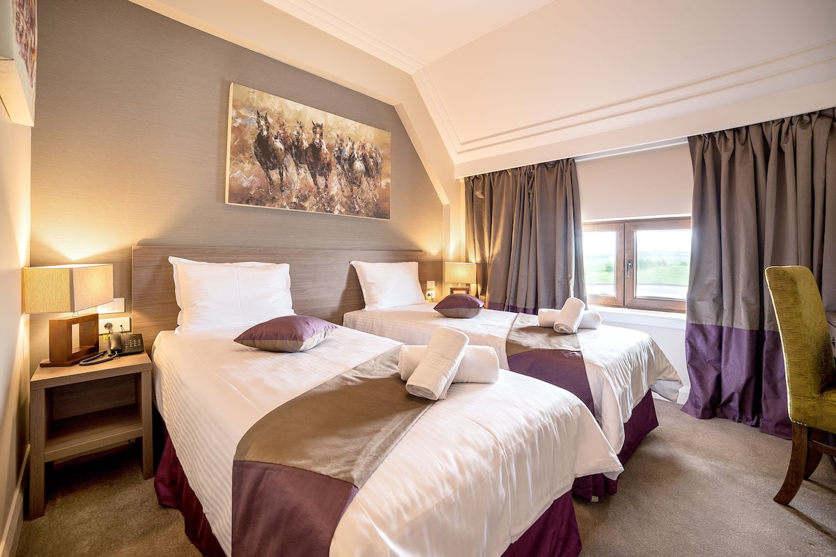 Quarto de hotel com duas camas, um quadro na parede, vista para o exterior e uma cadeira.