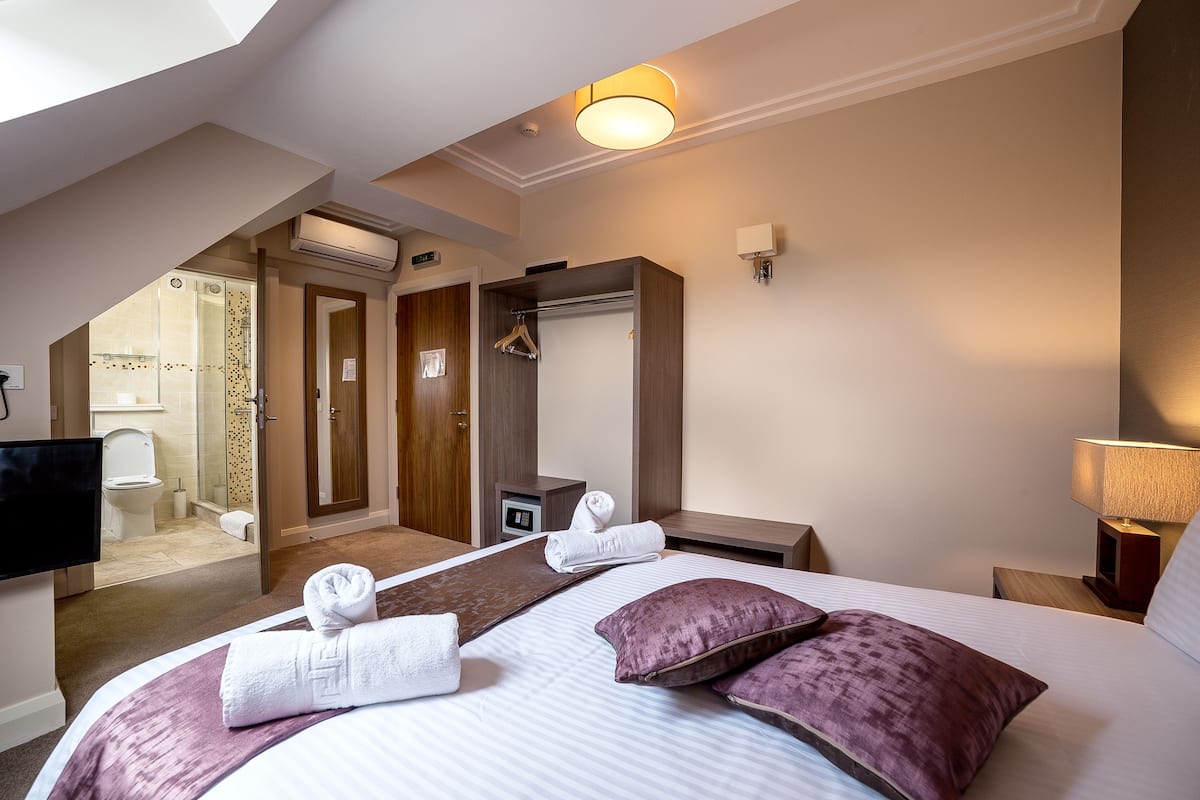 Quarto de hotel com uma cama grande, um closet espaçoso, banheiro com chuveiro e uma televisão.