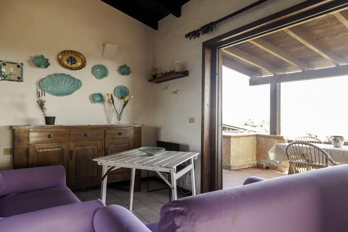 Ein Zimmer mit einem Holzkabinett, einem weißen Tisch, violetten Sofas und einem Balkon mit Blick.