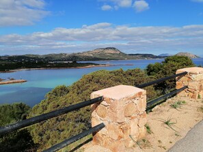 A coastal landscape with a stone railing, a clear view of the sea, and distant mountains.