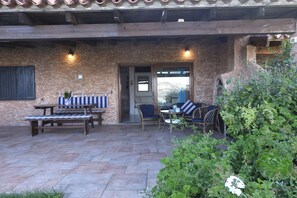 An outdoor patio area with stone flooring, wooden furniture, and a stone wall.