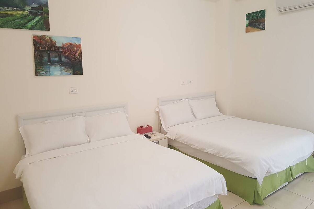 A room with two single beds, white bedding, a nightstand with a red box, and two paintings on the wall.