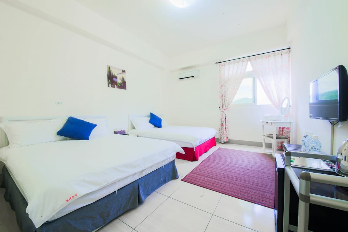 A hotel room with two beds, a desk with a chair, a television, and a window with curtains.
