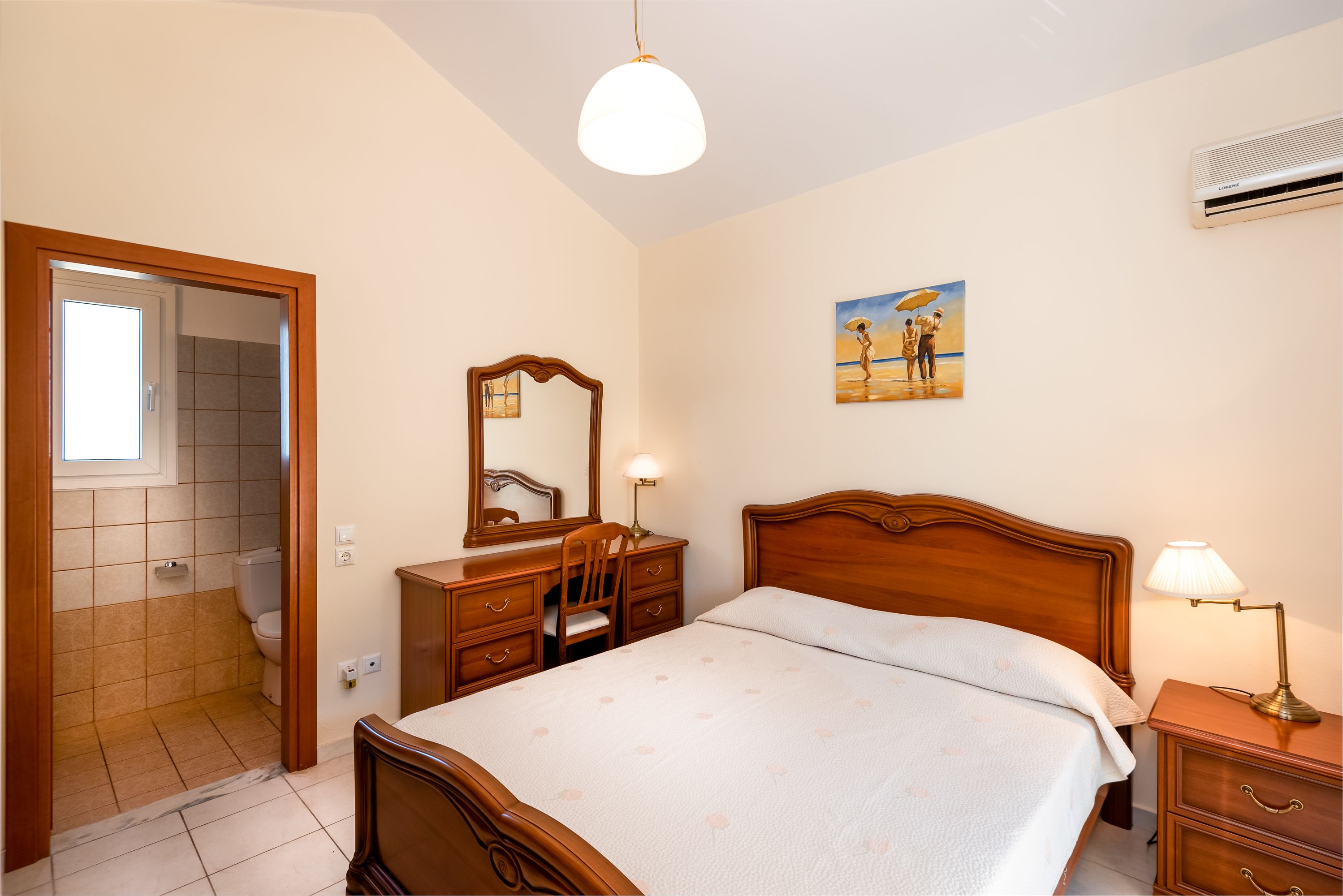 A bedroom with a wooden bed, a bedside table with a lamp, a dresser, a mirror, and a painting on the wall.