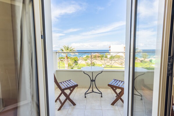 A balcony with a table and two chairs, overlooking a garden and the sea. - Pela Sofia (Hersonissos)