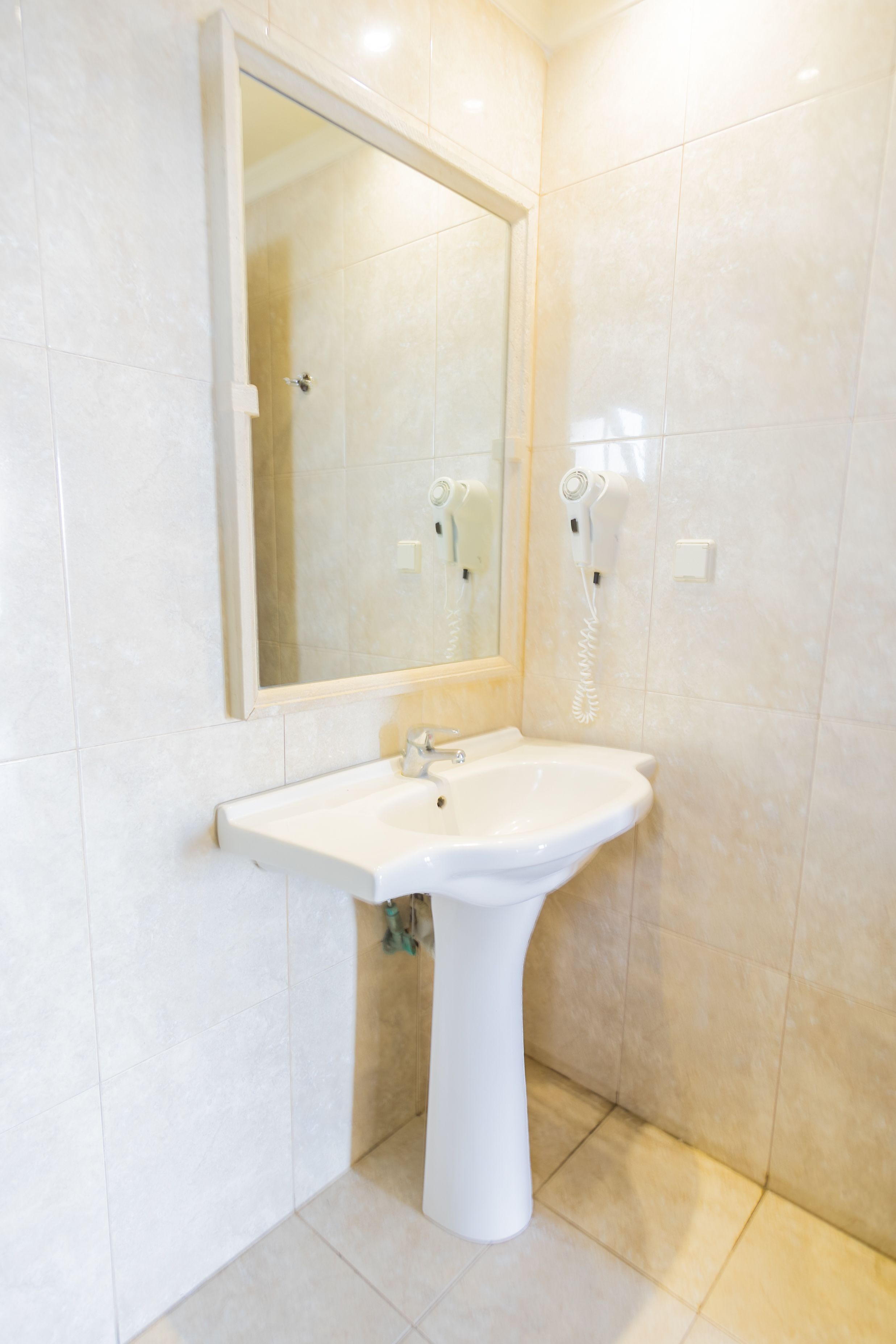 Un bany amb un lavabo pedestal, un mirall i un assecador de cabells fixat a la paret.