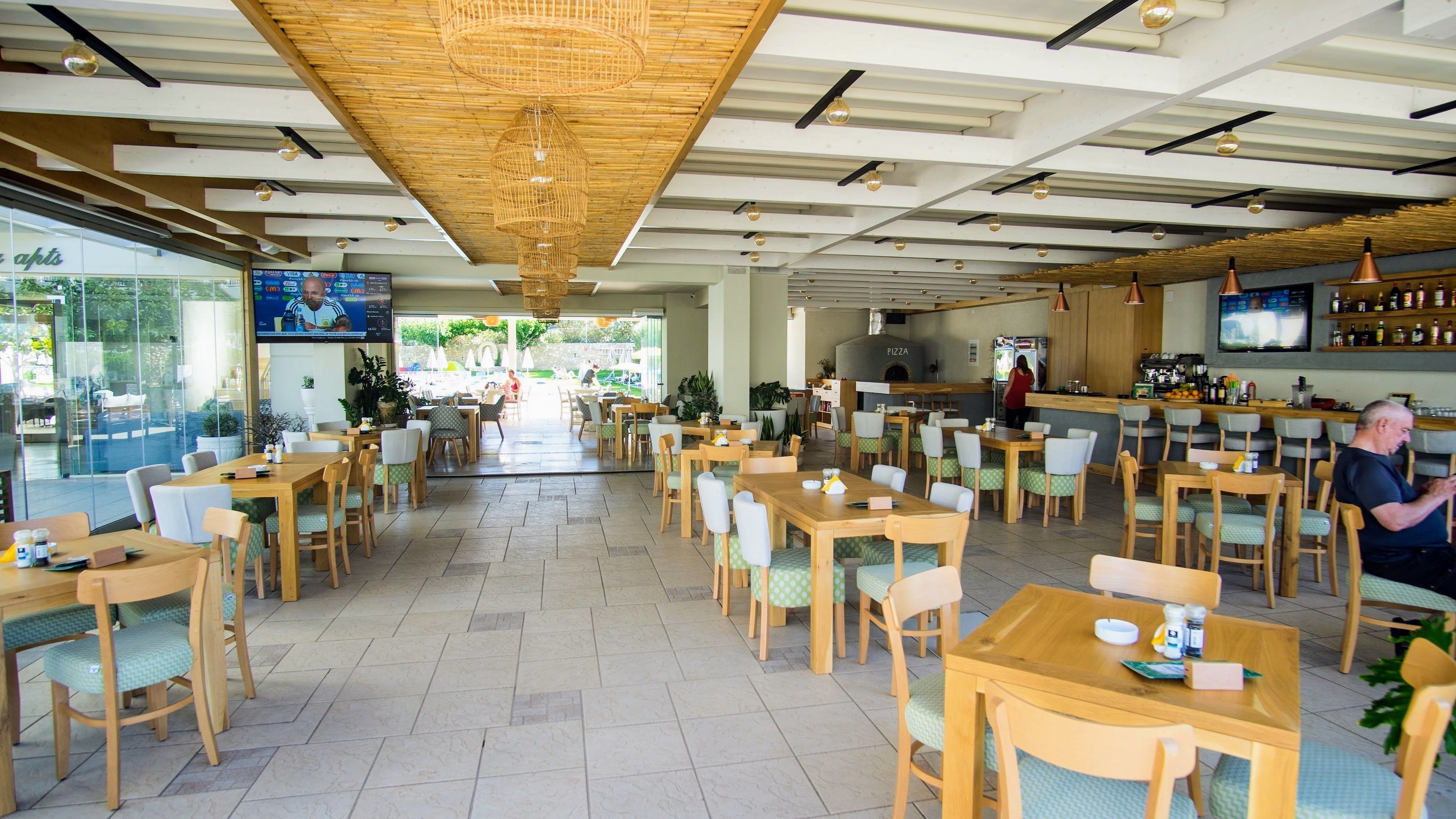 Un restaurant espaiós amb taules i cadires de fusta, una zona de bar i una pantalla gran que mostra contingut.