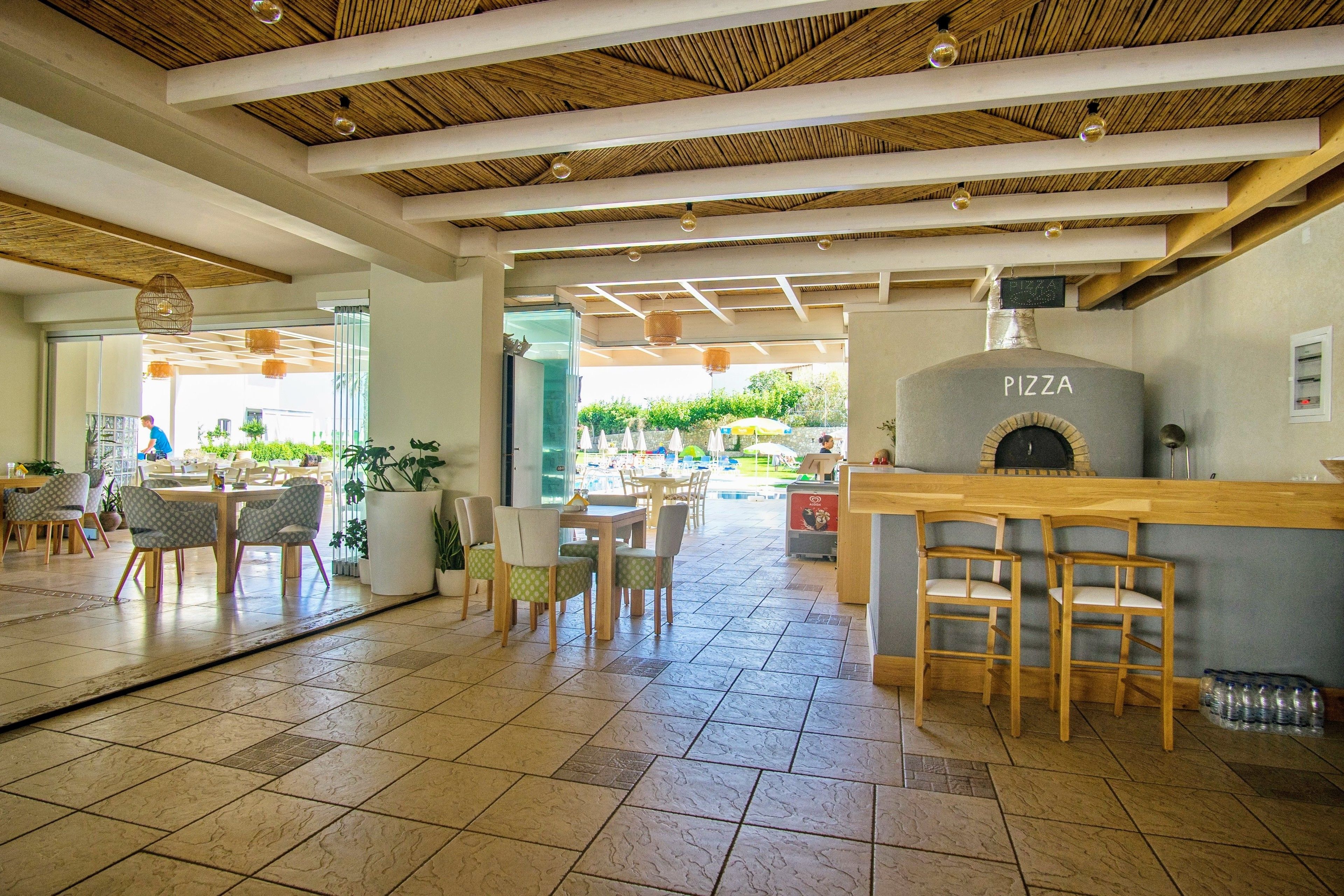 A restaurant with a pizza oven, wooden ceiling, and tiled flooring.