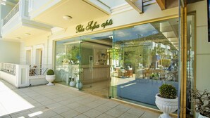 A hotel entrance with a glass facade, a reception desk, and potted plants. - Pela Sofia (Hersonissos)