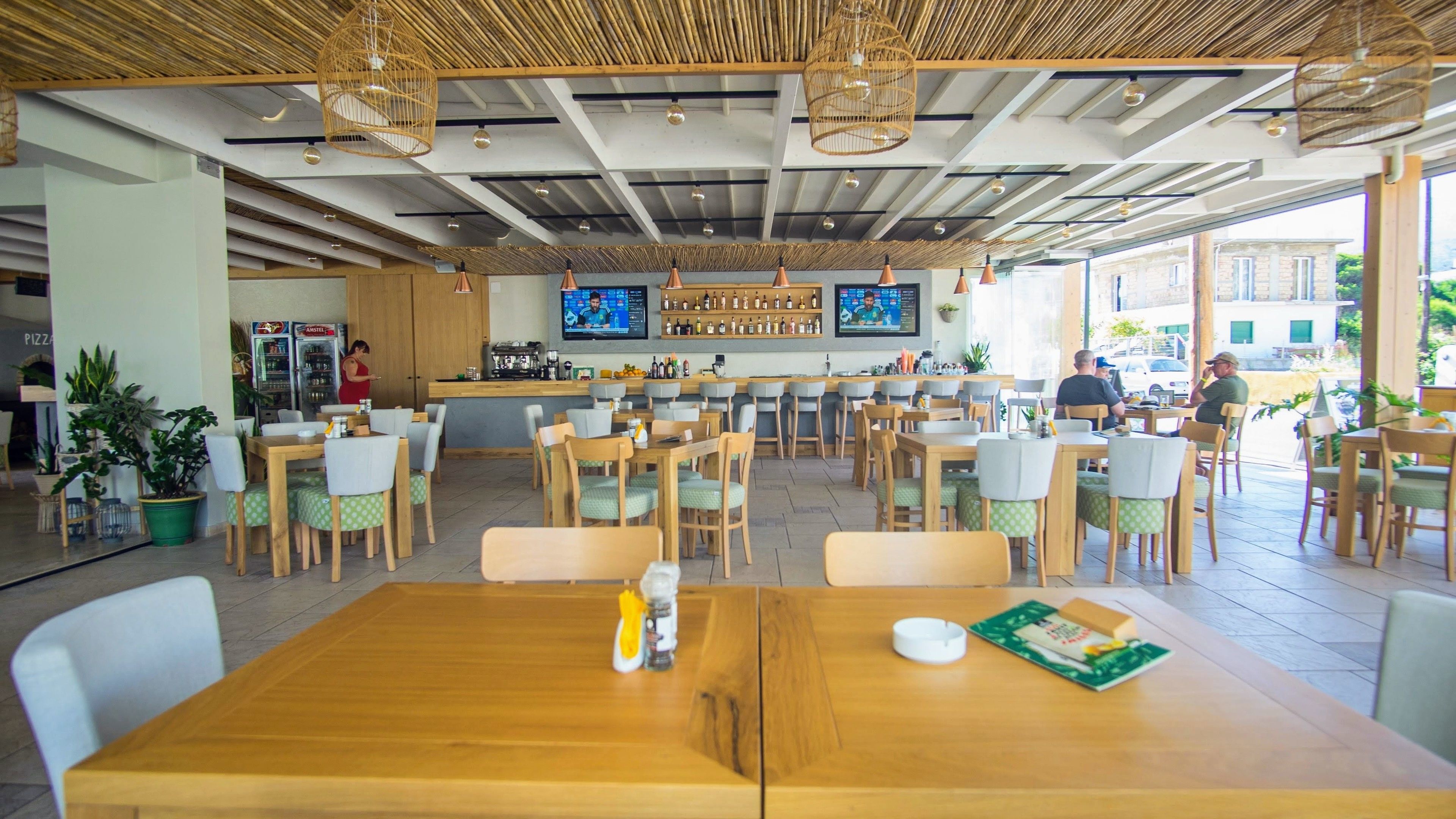 Un restaurante con mesas y sillas de madera, una zona de bar y ventanas amplias.