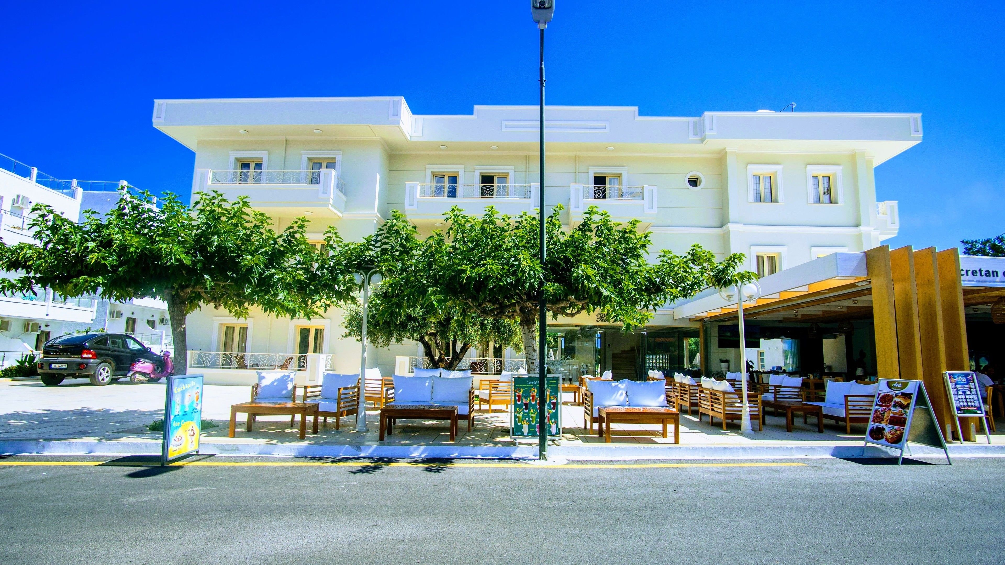 A hotel with a white facade, outdoor seating area, and a signboard.