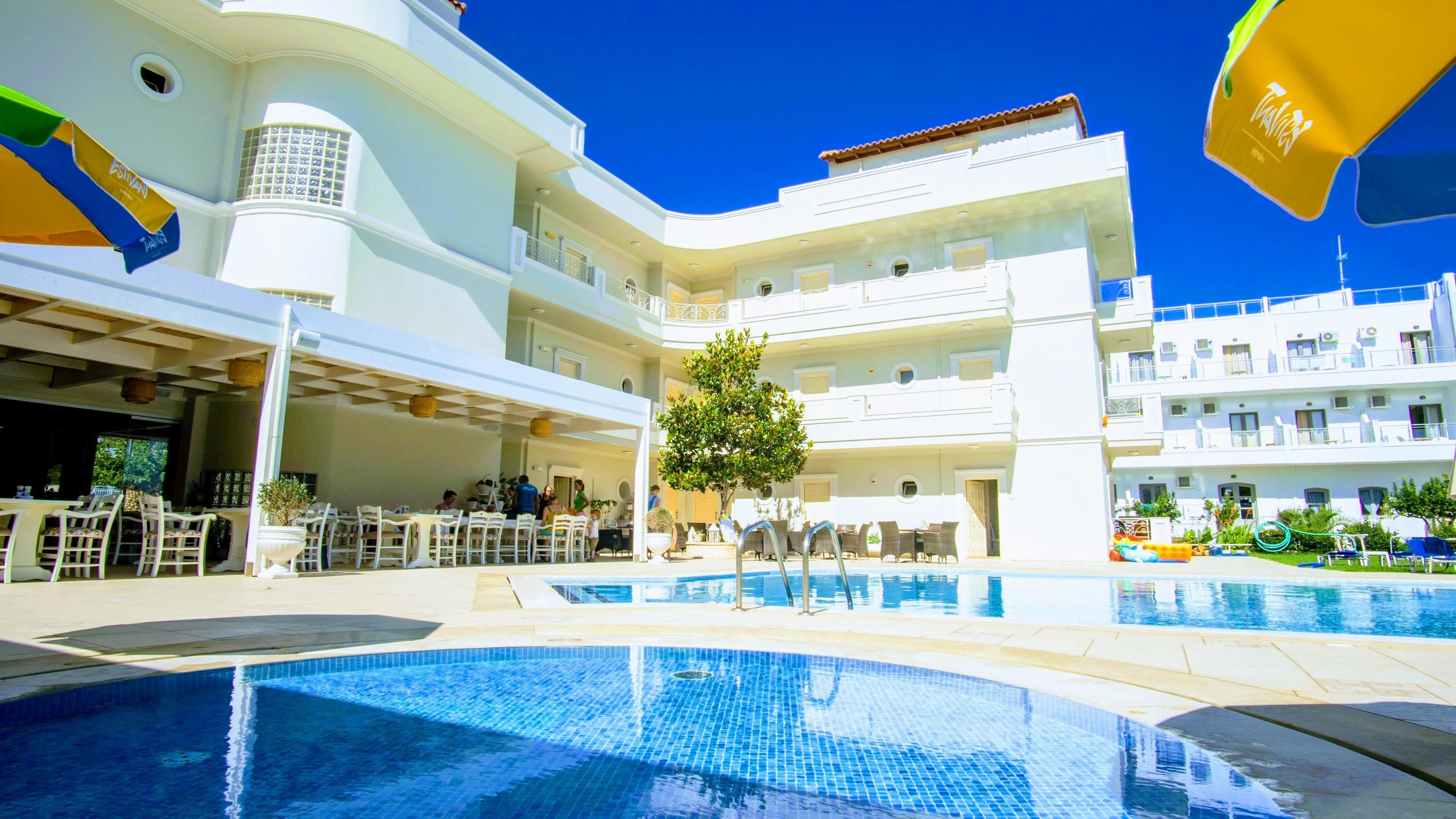 A hotel with multiple swimming pools, outdoor seating areas, and a central tree.