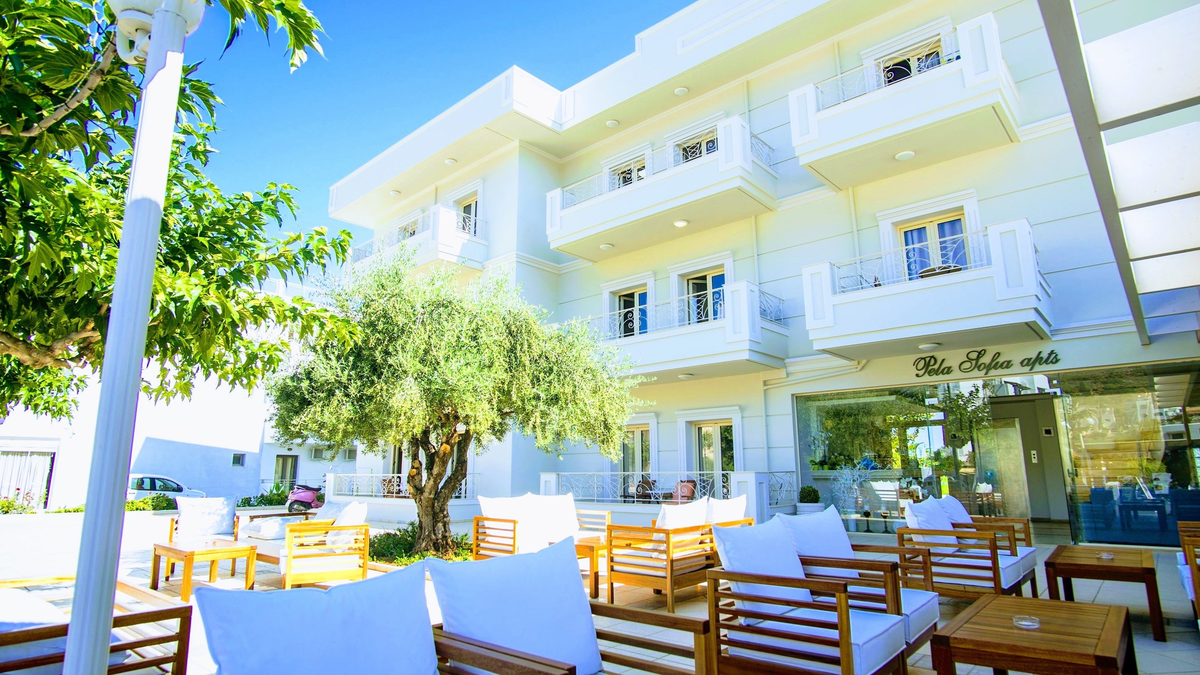 Un hôtel doté d’une terrasse, d’un arbre et d’une enseigne indiquant « Pela Sofa apts ».