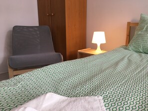 A hotel room with a bed, a chair, a nightstand with a lamp, and a wooden wardrobe. - Visit Lublin Apartments Plus Skłodowskiej (Lublin)