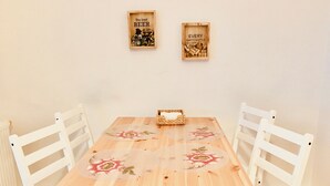 Une table à manger en bois, recouverte de nappes à motifs floraux, entourée de chaises blanches, dans une pièce aux murs de couleur neutre.