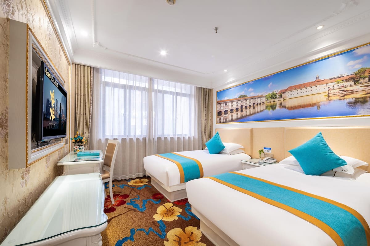 A hotel room with two beds, a desk, a TV, and a large window.