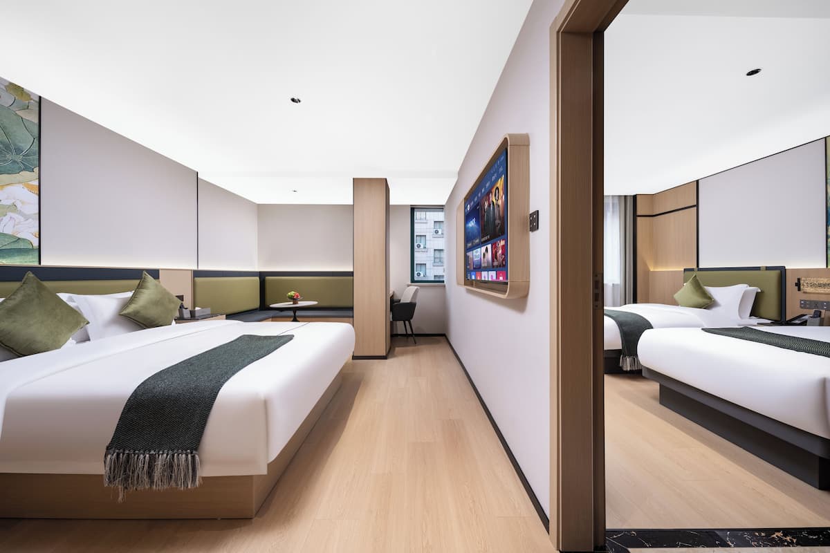 A hotel room with two beds, a desk, and a large digital screen on the wall.