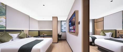 A hotel room with two beds, a desk, and a large digital screen on the wall.