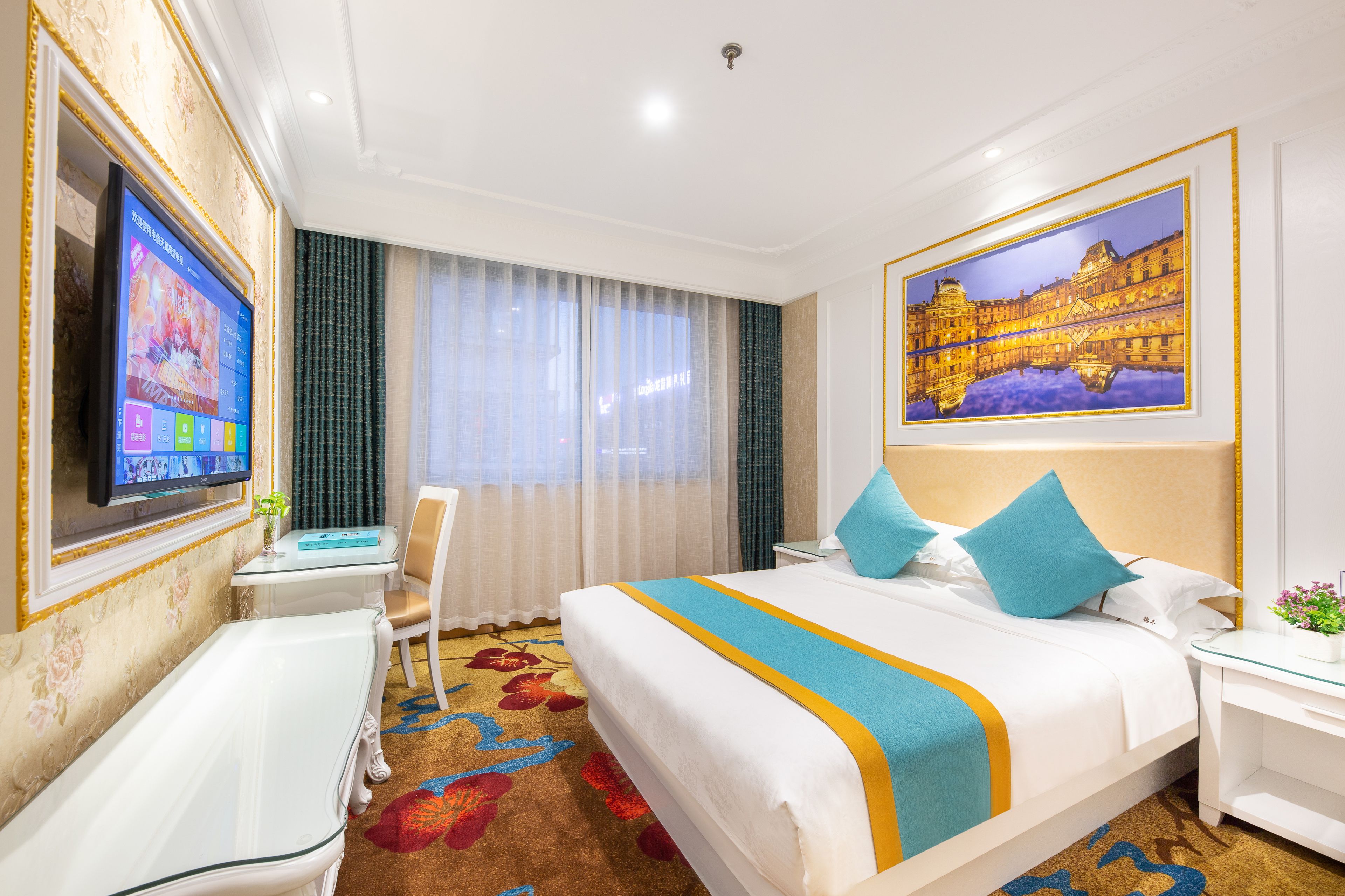 A hotel room with a large bed, a TV mounted on the wall, a desk, and a chair.