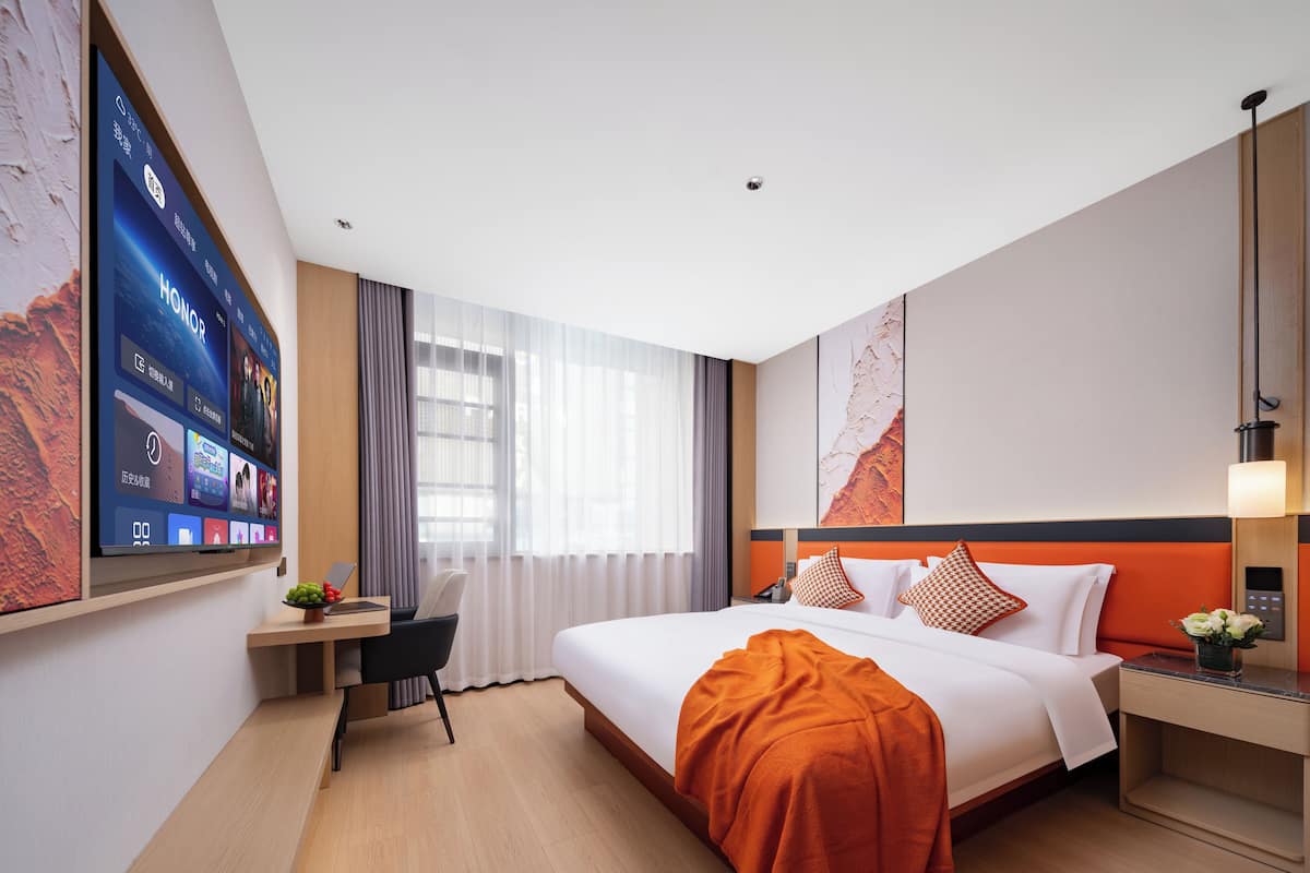 A modern hotel room with a large bed, a desk, and a flat-screen TV mounted on the wall.