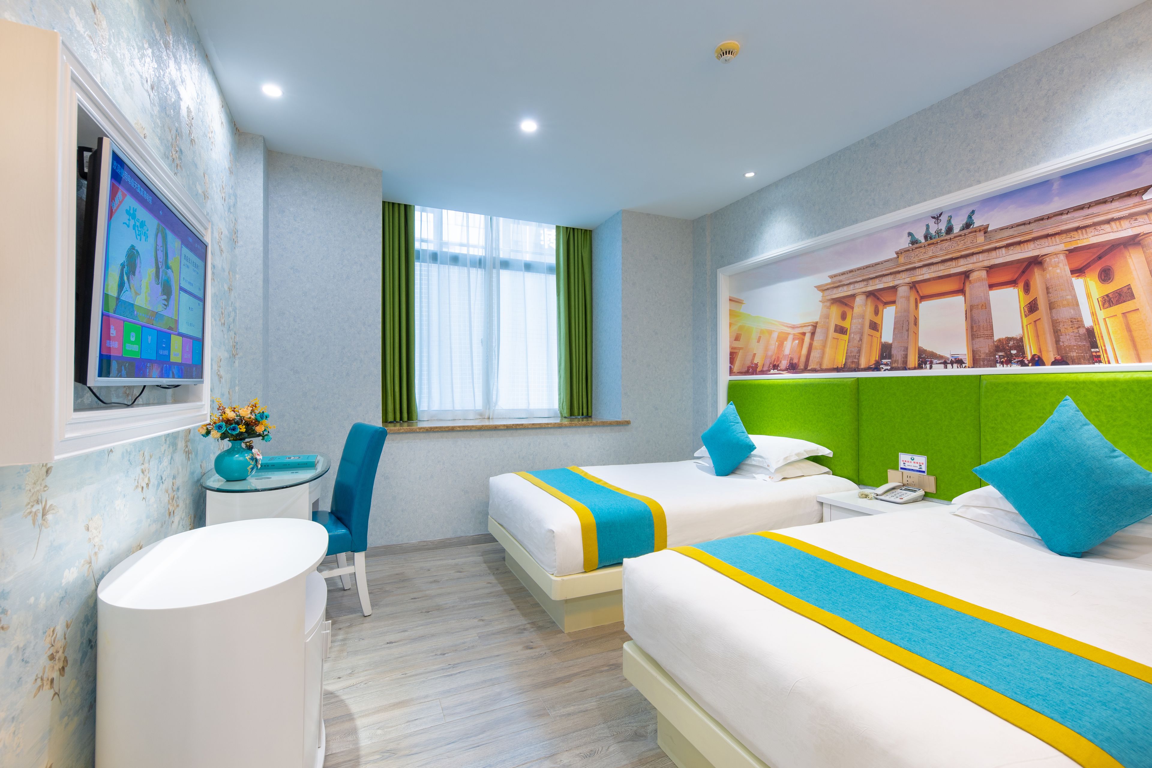 A hotel room with two beds, a desk, a chair, a TV, and a window with curtains.