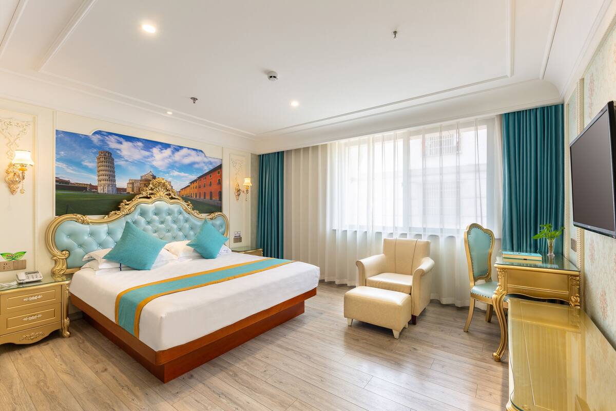 A hotel room with a large bed, a desk, a chair, and a television.