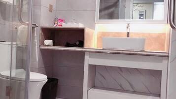 Uma casa de banho moderna com chuveiro em cabine de vidro, sanita branca, toucador com espelho e lavatório.