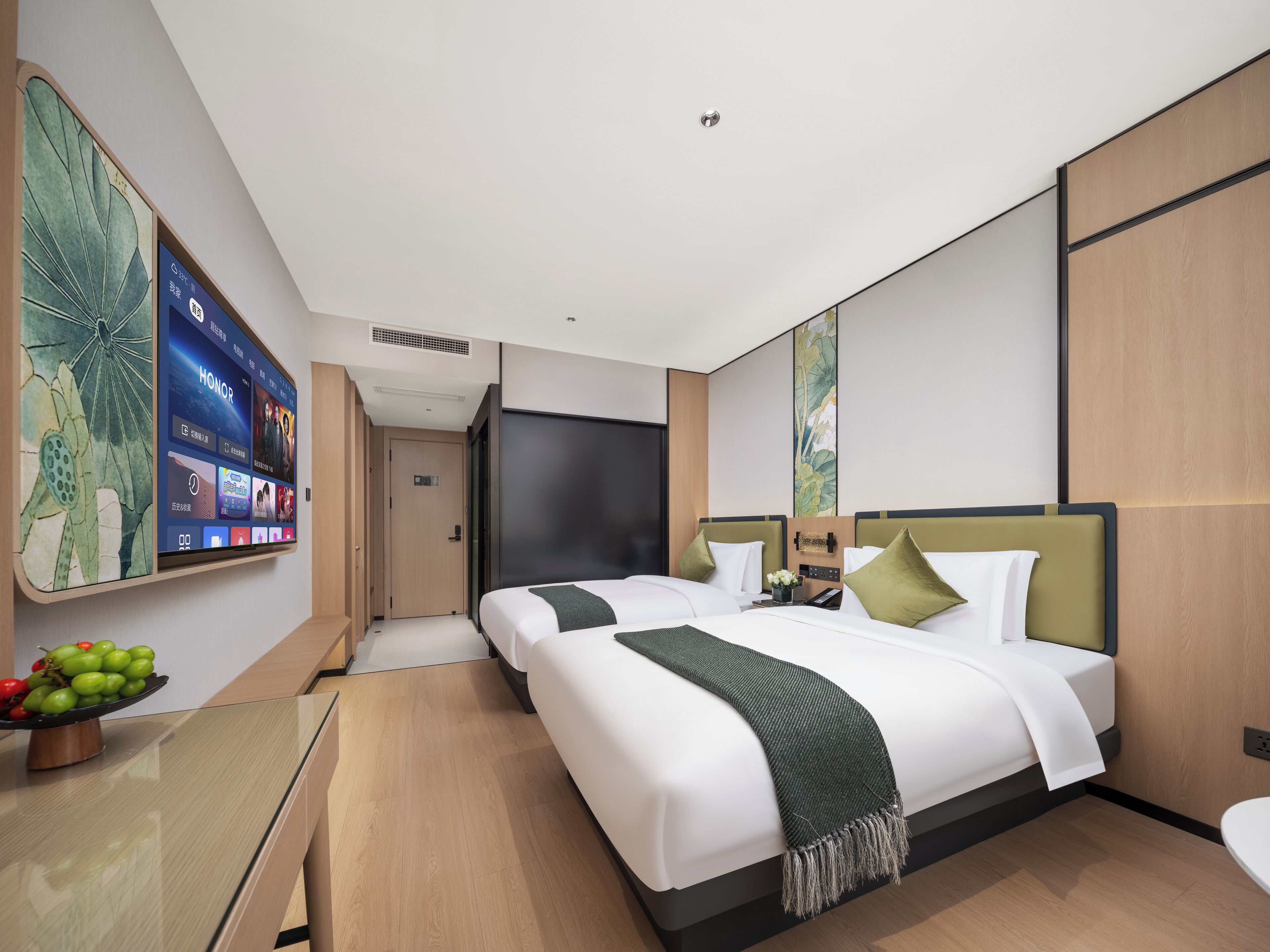 Una habitación de hotel moderna con dos camas, una pantalla digital grande en la pared y una pequeña mesa con fruta.