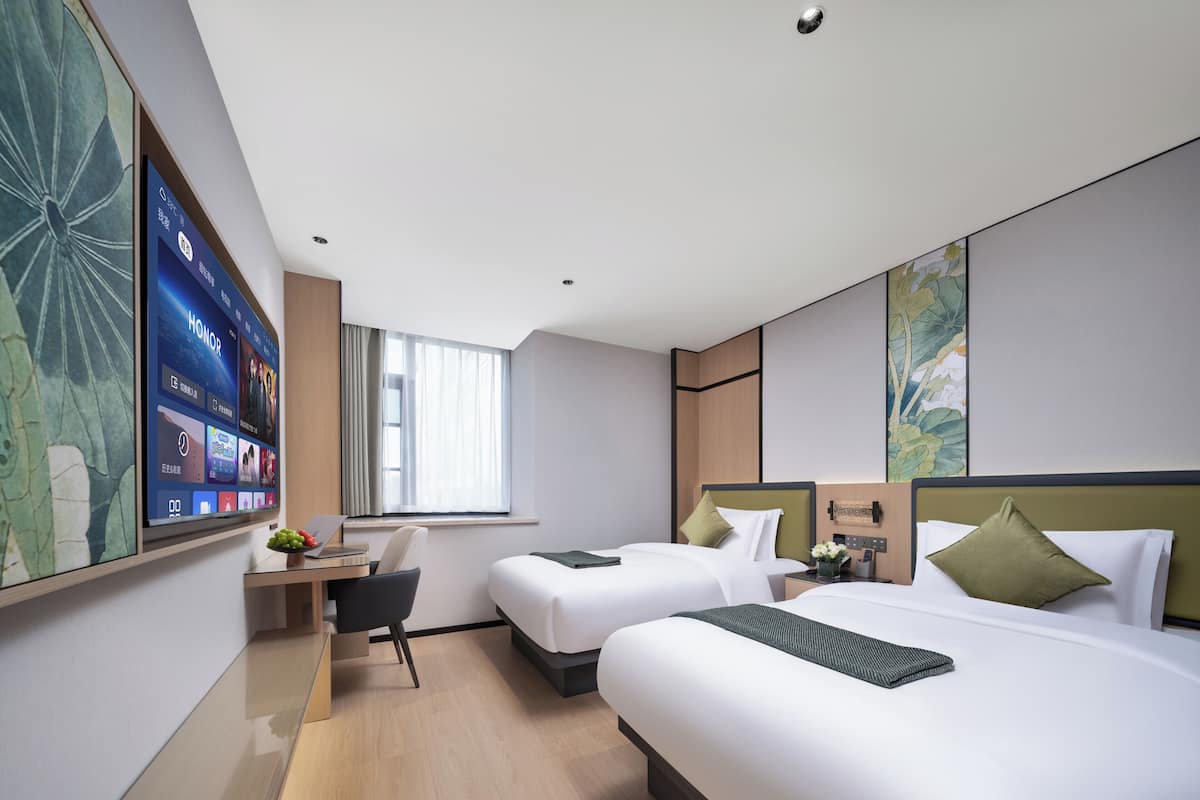 A modern hotel room with two beds, a desk, and a large flat-screen TV mounted on the wall.