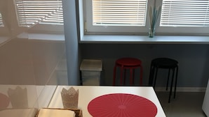 Un coin repas avec une table dressée pour deux personnes, agrémenté d’un panier tressé et de deux sets de table rouges.