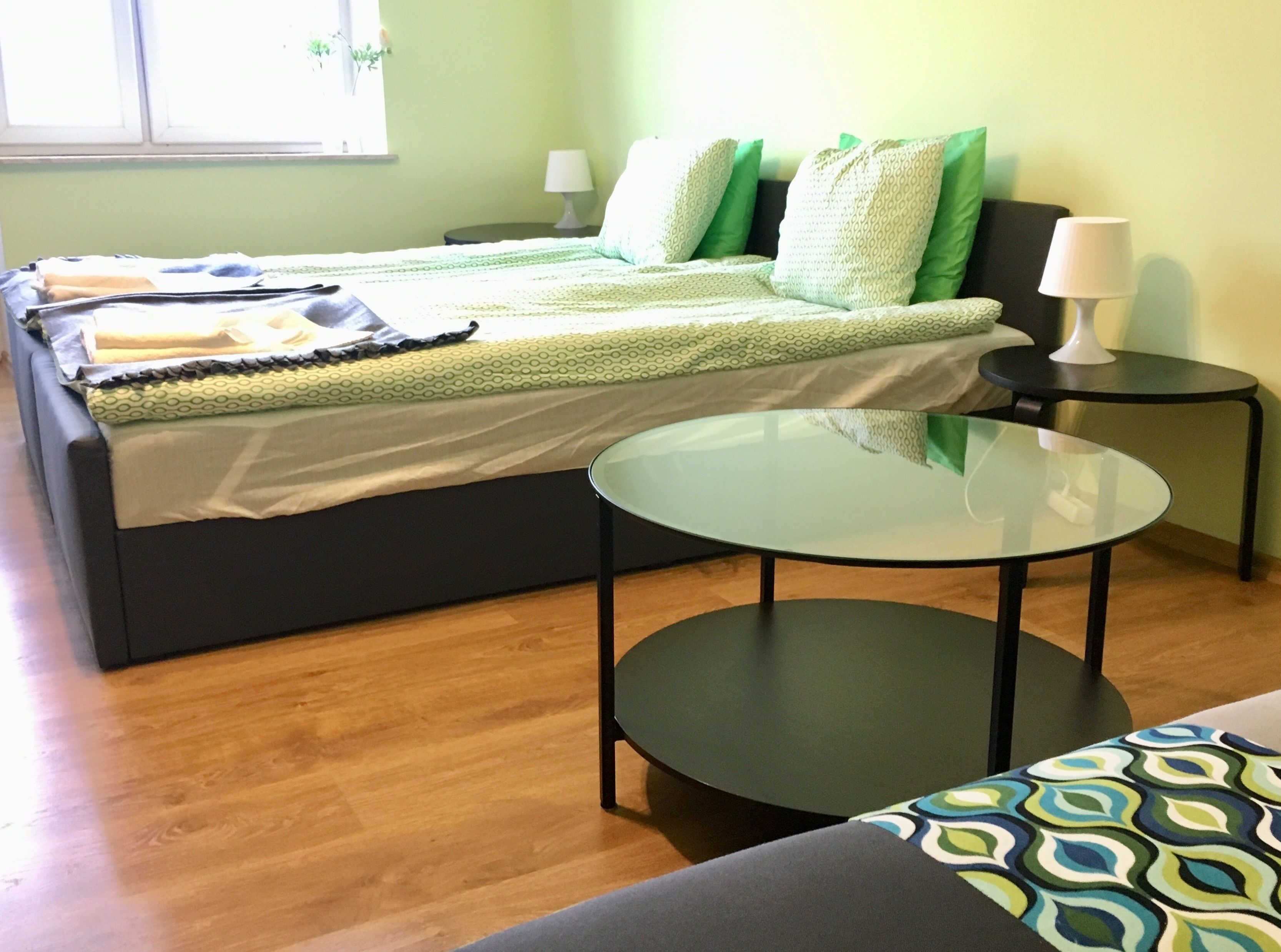 A modern bedroom with a bed, bedside tables, a glass table, and a patterned sofa.