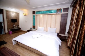 Une chambre d’hôtel avec un grand lit, un téléviseur à écran plat fixé au mur, une table de chevet avec une lampe et un miroir.