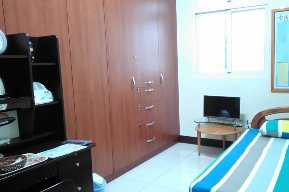 A bedroom with a bed, a desk, a wardrobe, a TV, and a window.
