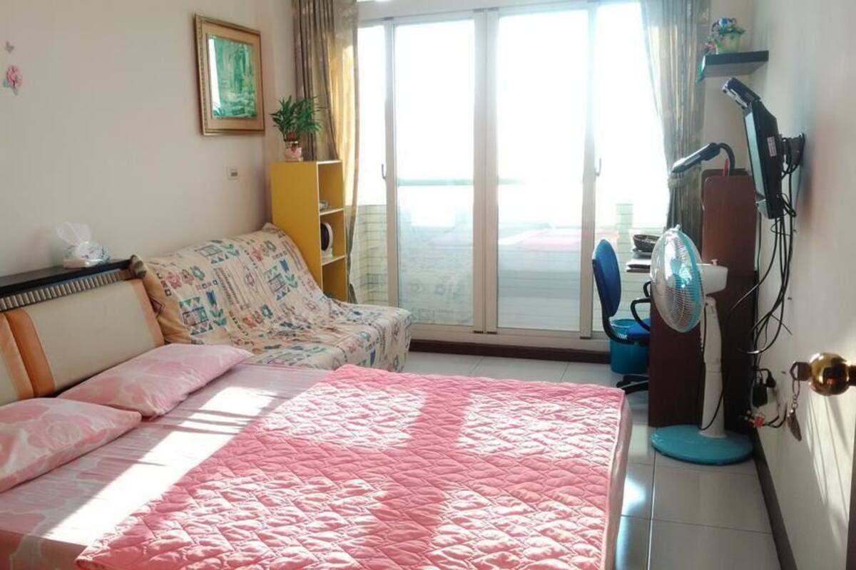 A bedroom with a bed, a sofa, a desk, and a window.