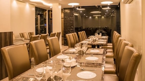 A long dining table set with plates, glasses, and cutlery, flanked by leather chairs in a modern dining area with marble accents and recessed lighting. - Grand Paradise (Port Blair)