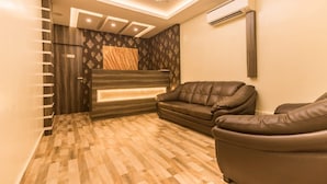 A modern room with a wooden floor, a brown leather sofa, a built-in bench, and a ceiling light fixture. - Grand Paradise (Port Blair)