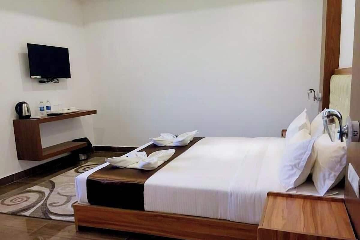 A hotel room with a bed, a TV, a wooden shelf with toiletries, and a bathroom.