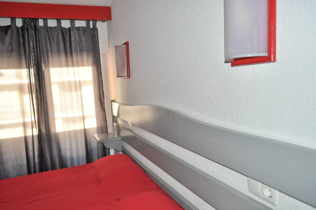 A hotel room with a bed, a nightstand, a mirror, and a window with curtains.