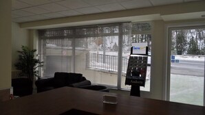 Ein Empfangsbereich mit einer Rezeption, einer Pflanze, einem schwarzen Sofa und einem Fenster mit Jalousien.