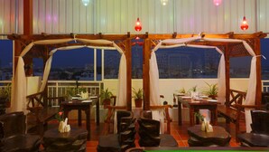 A rooftop restaurant with wooden furniture, tables set for dining, and potted plants.