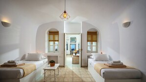 Quarto de hotel com duas camas, uma mesinha e vista para a cozinha através de uma porta aberta.