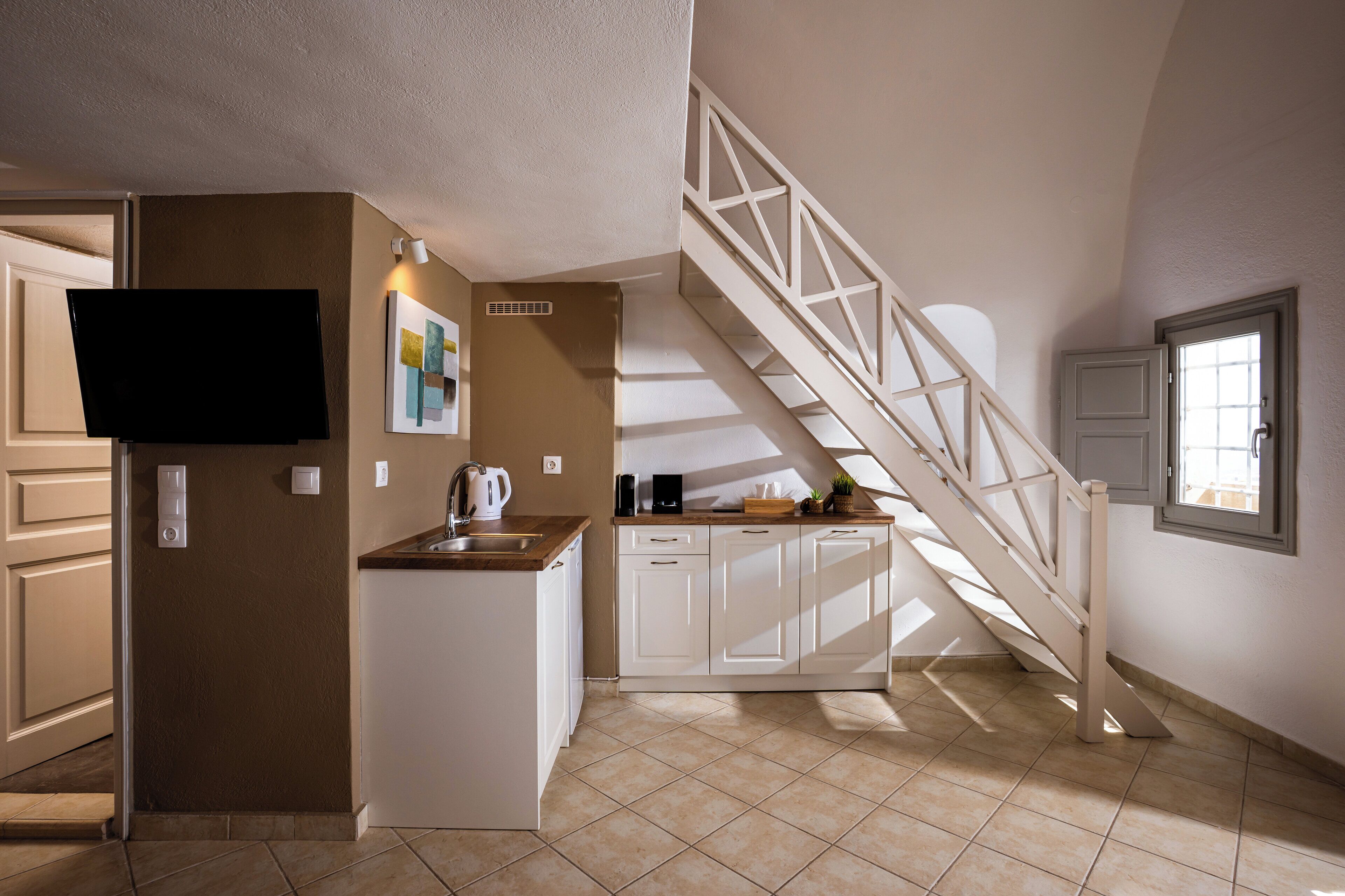 A kitchen with a built-in refrigerator, a flat-screen TV, a coffee maker, and a window overlooking a staircase.