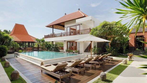 Une maison moderne à deux étages, dotée d’une piscine, de chaises longues et d’un jardin bien entretenu.