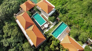Vue aérienne d’un complexe hôtelier comprenant plusieurs bâtiments, une piscine et une végétation luxuriante.